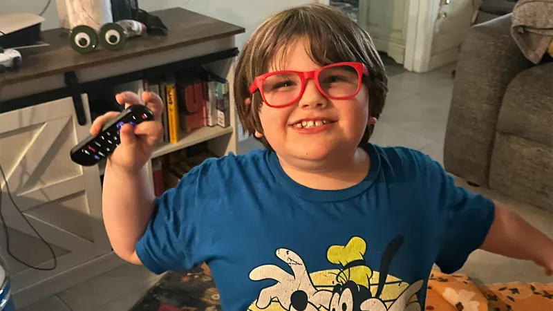 little boy with glasses waving his arms with a tv remote in his hand