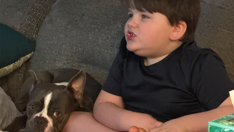 little boy and his dog sitting on the couch at home eating a snack