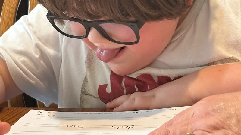 young autistic boy working on schoolwork with his tutor